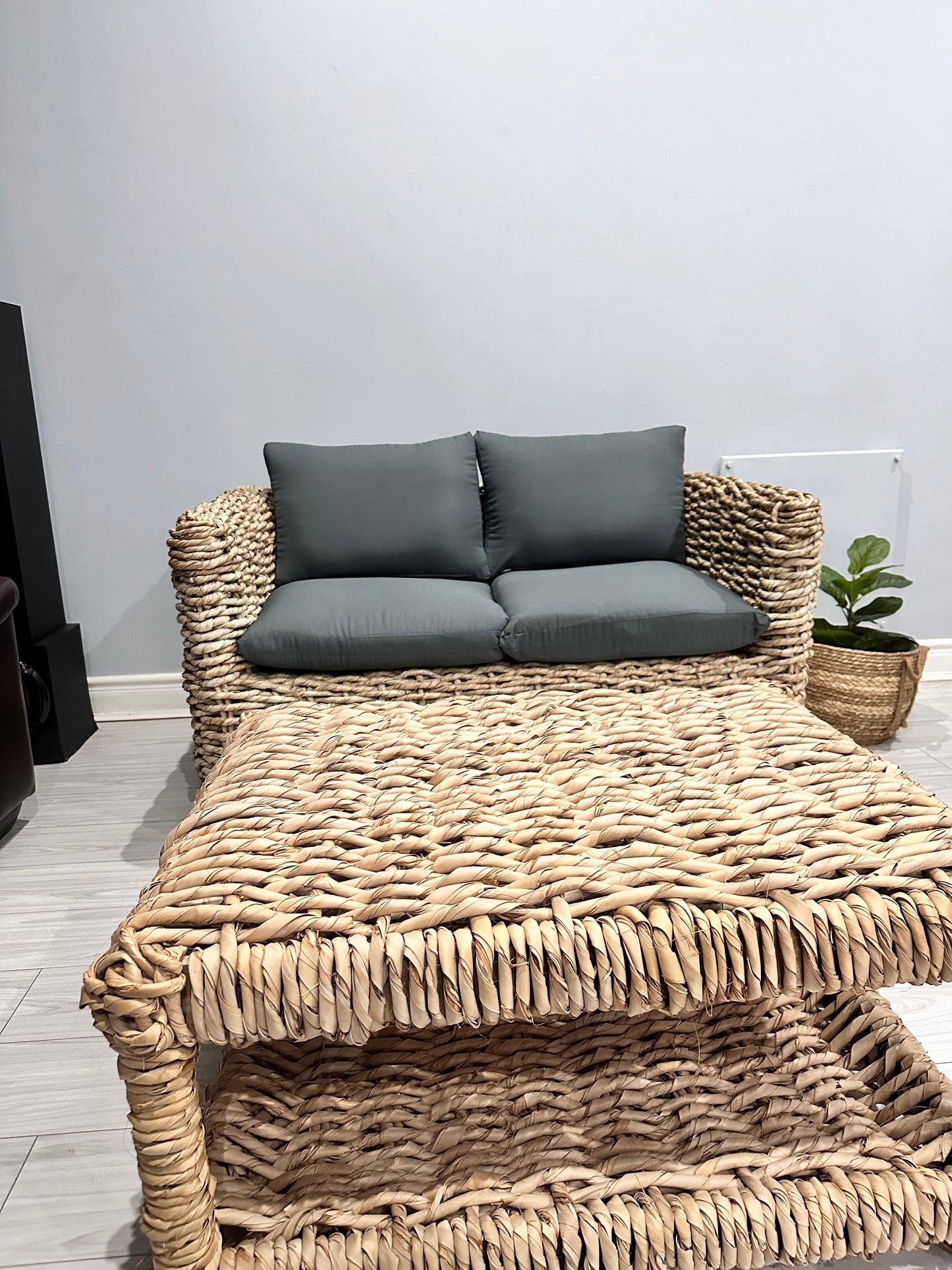 Wicker coffee table with 2-seater wicker couch surrounding it in grey cushions