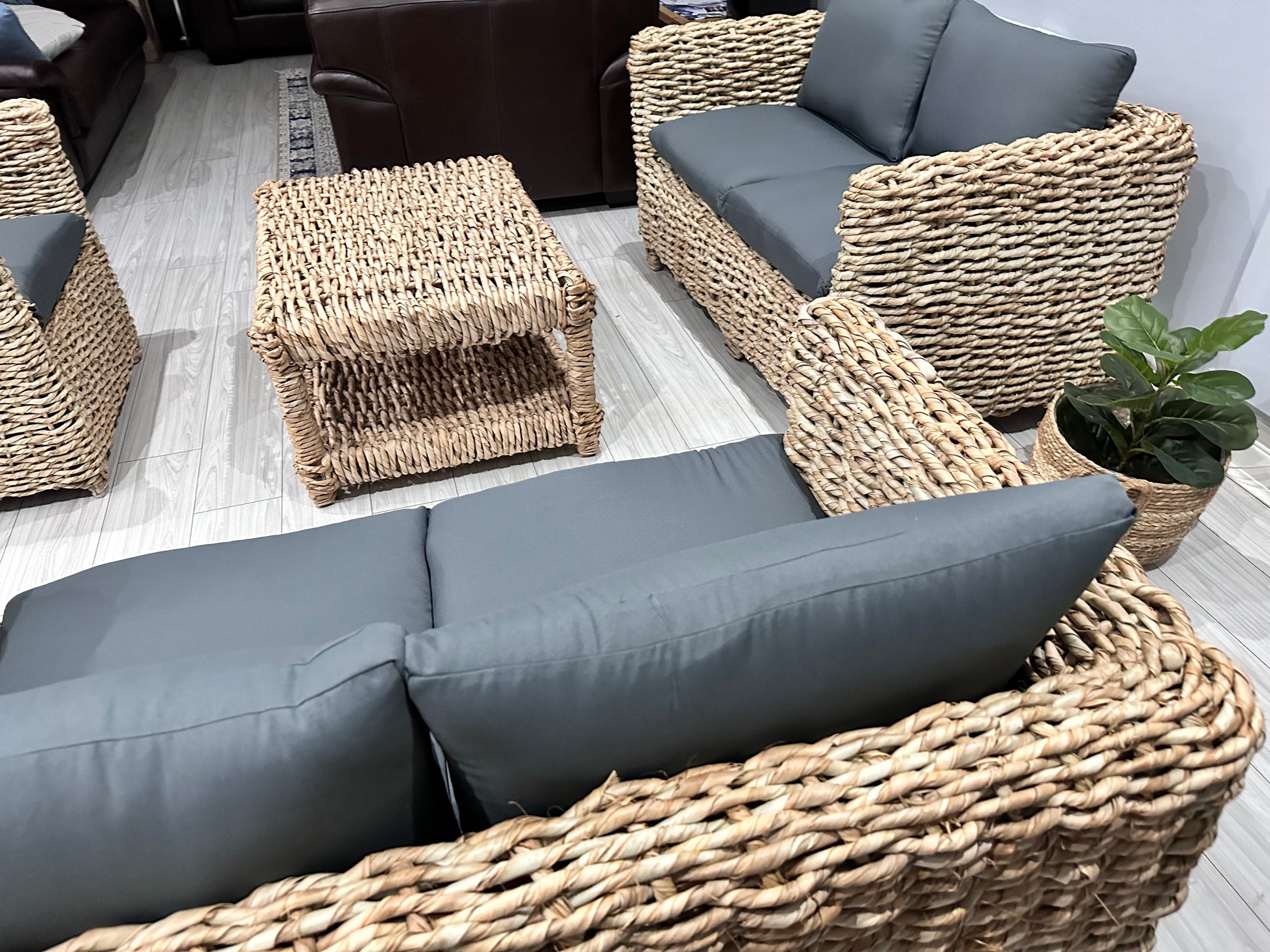 Wicker coffee table with wicker couches surrounding it in grey cushions