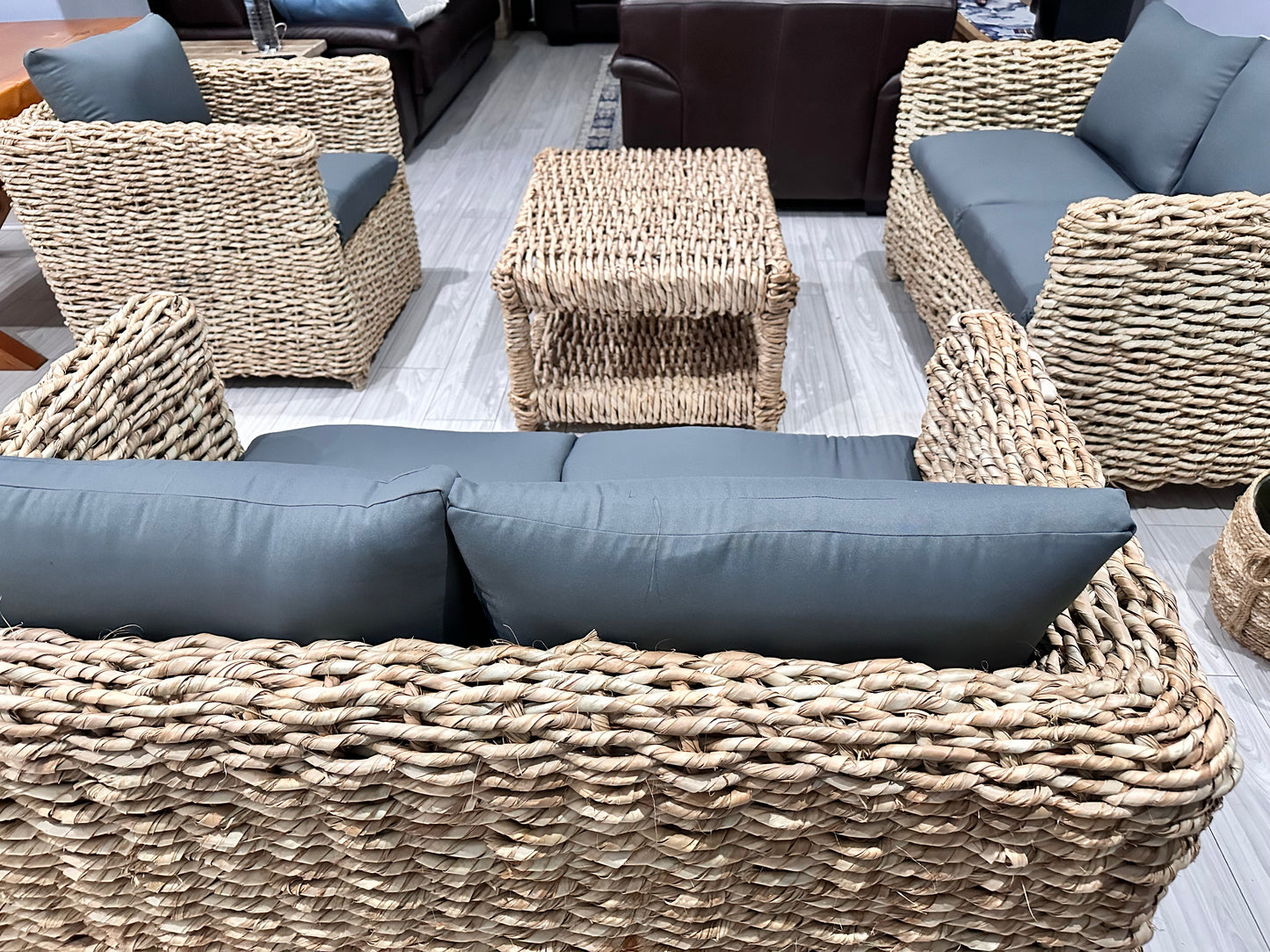 Wicker coffee table with wicker couches surrounding it in grey cushions