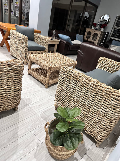 Wicker coffee table with wicker couches surrounding it in grey cushions