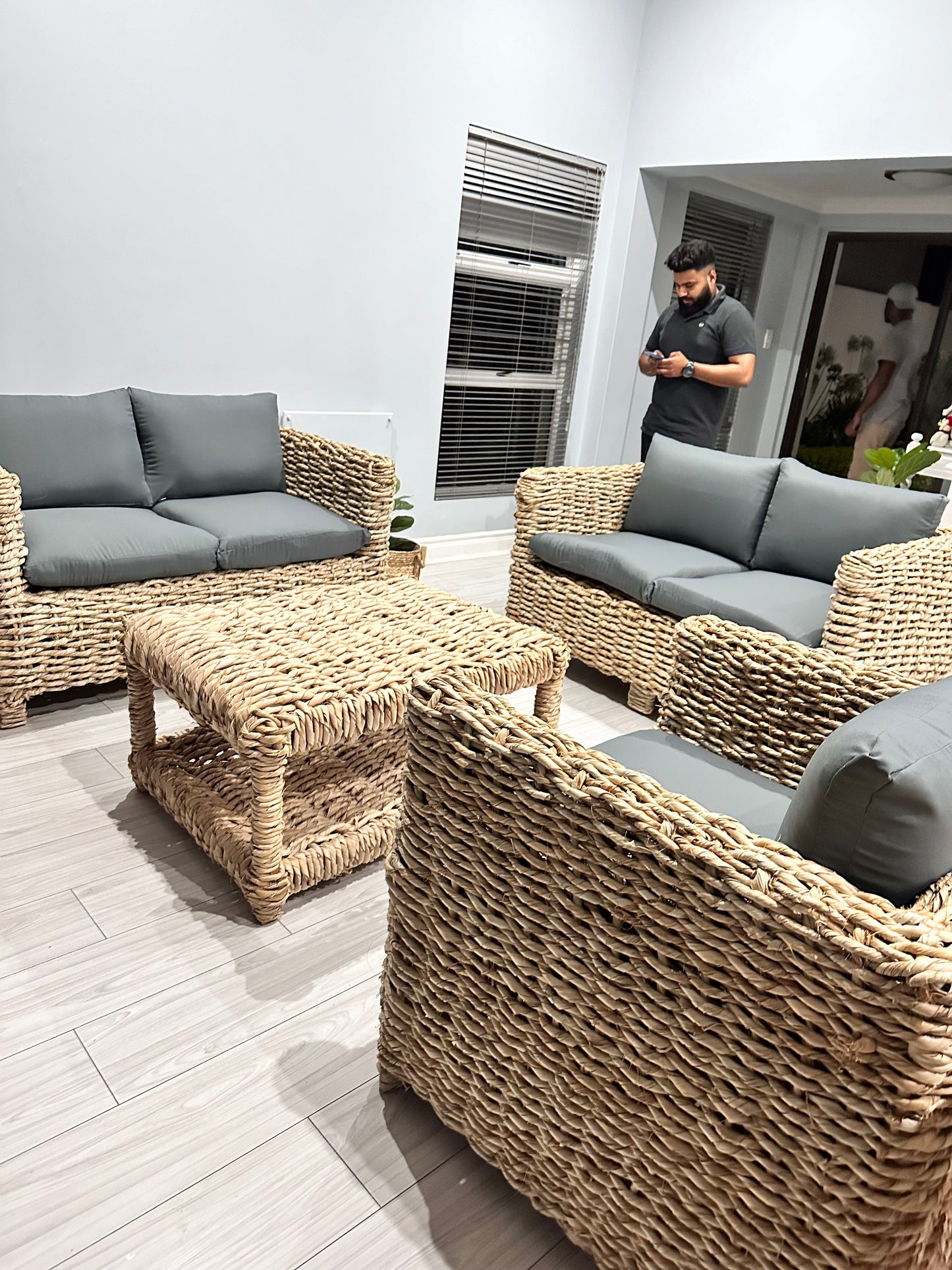 Wicker coffee table with wicker couches surrounding it in grey cushions