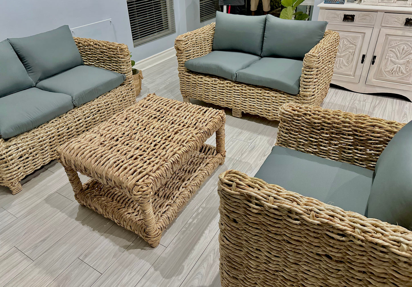 Wicker coffee table with wicker couches surrounding it in grey cushions